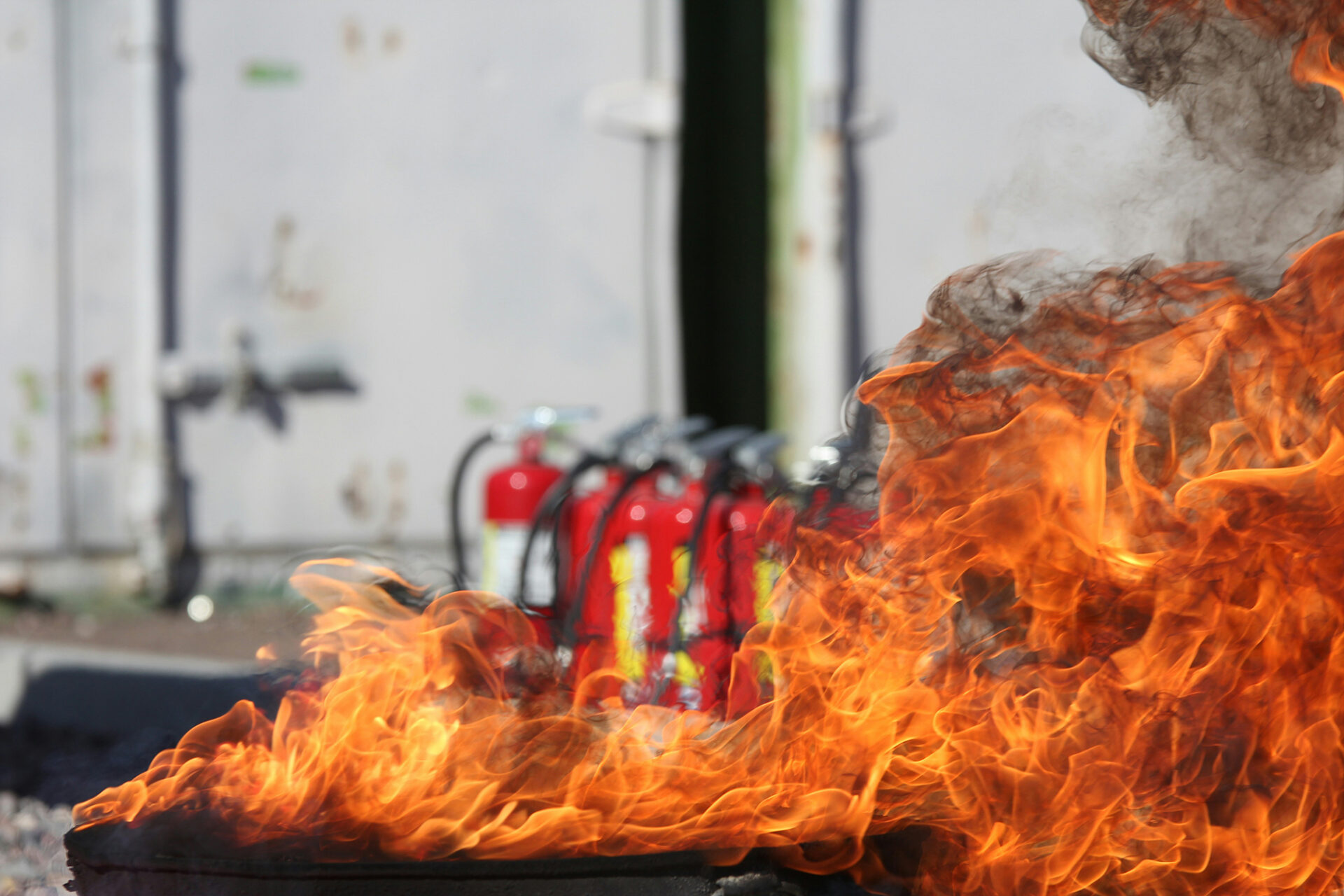 Eldsflammor med brandsläckare i bakgrunden under utbildning av brandskyddsansvarig